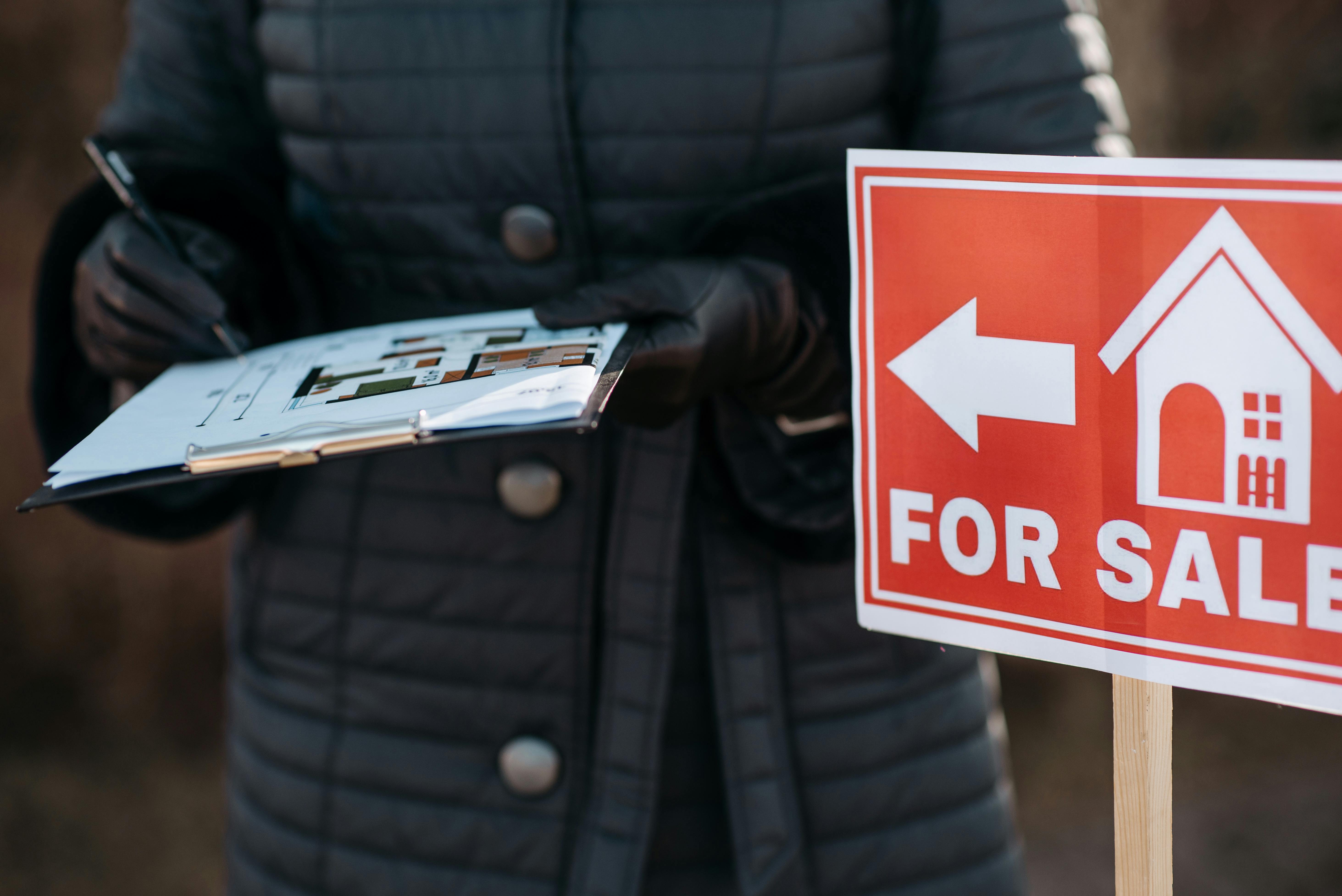 A woman holding a real estate for sale sign