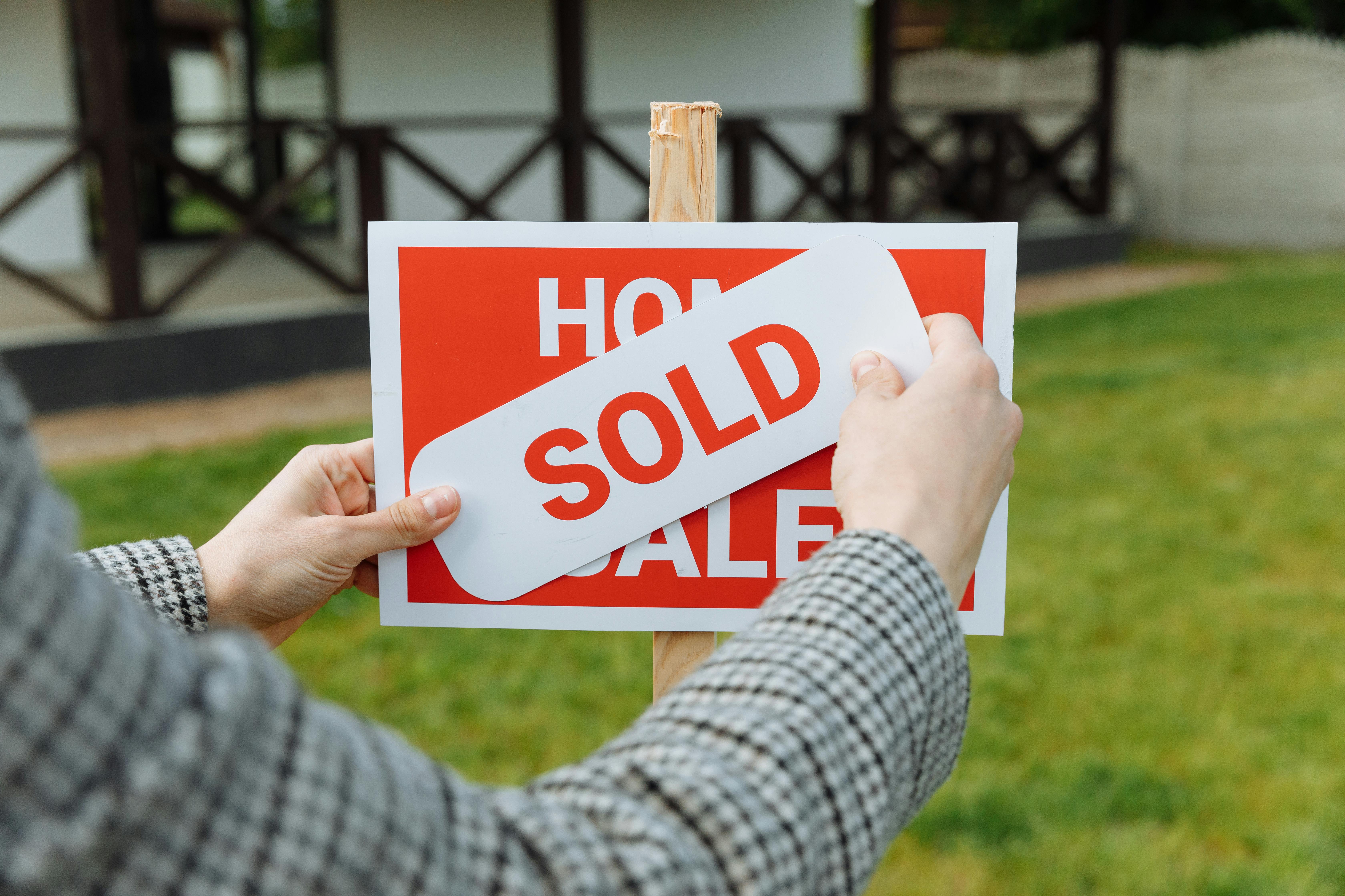 A person holding a sold sign in front of a house